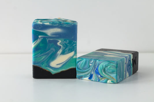 Two bars of marbled soap with blue and green patterns on a white background