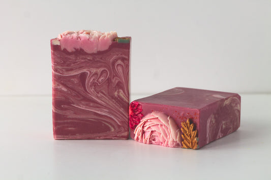 Two bars of marbled soap with gold adornments and hand piped soap flowers on a white background