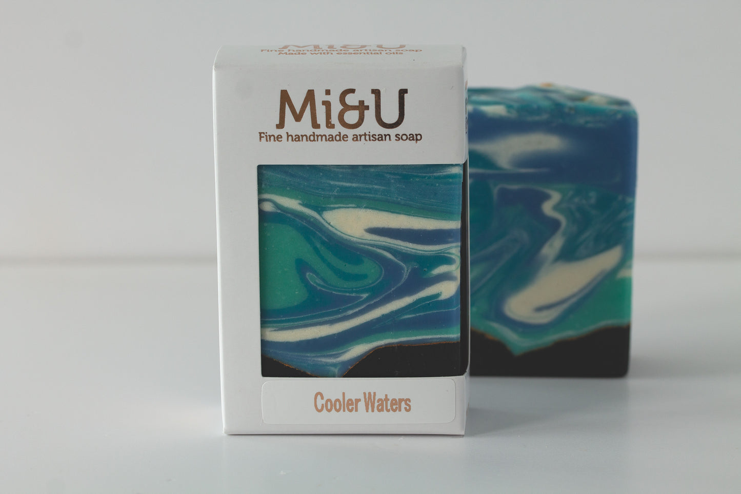 Mi&U handmade artisan soap with a blue and green swirl pattern next to its packaging on a white background