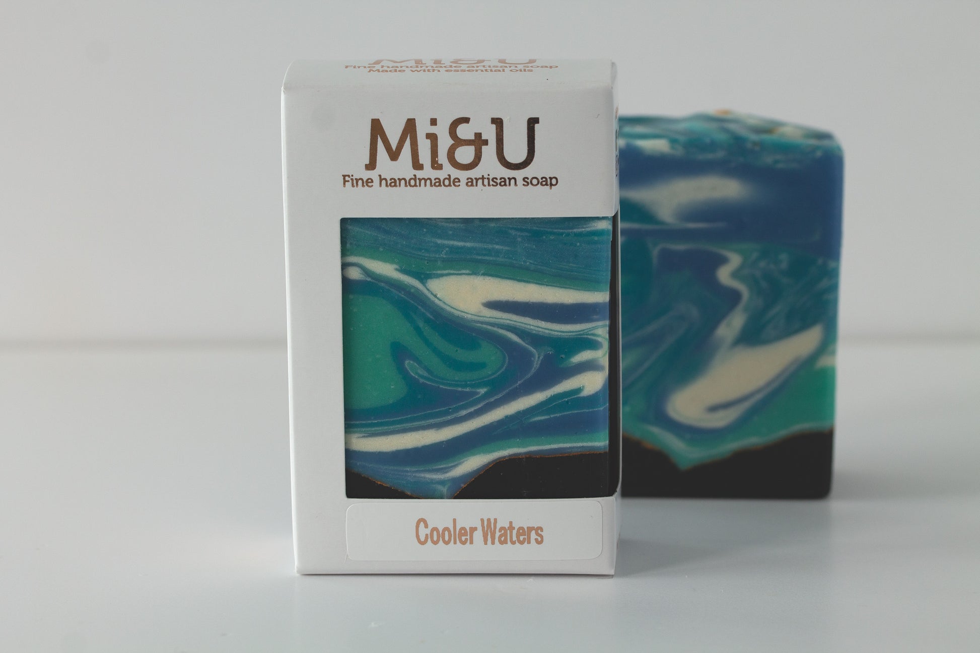 Mi&U handmade artisan soap with a blue and green swirl pattern next to its packaging on a white background