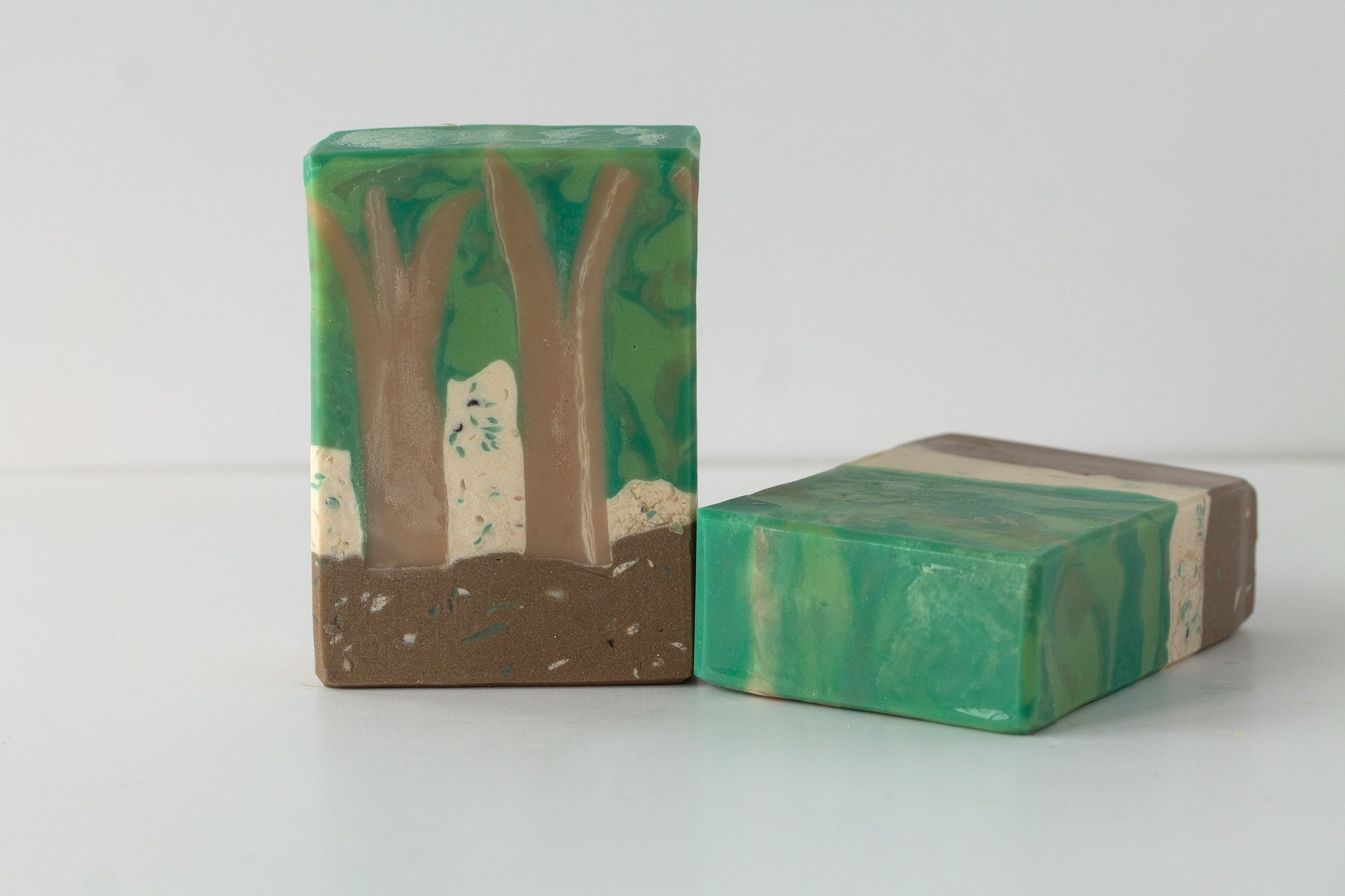 Two green and brown forest soap bars on a white background