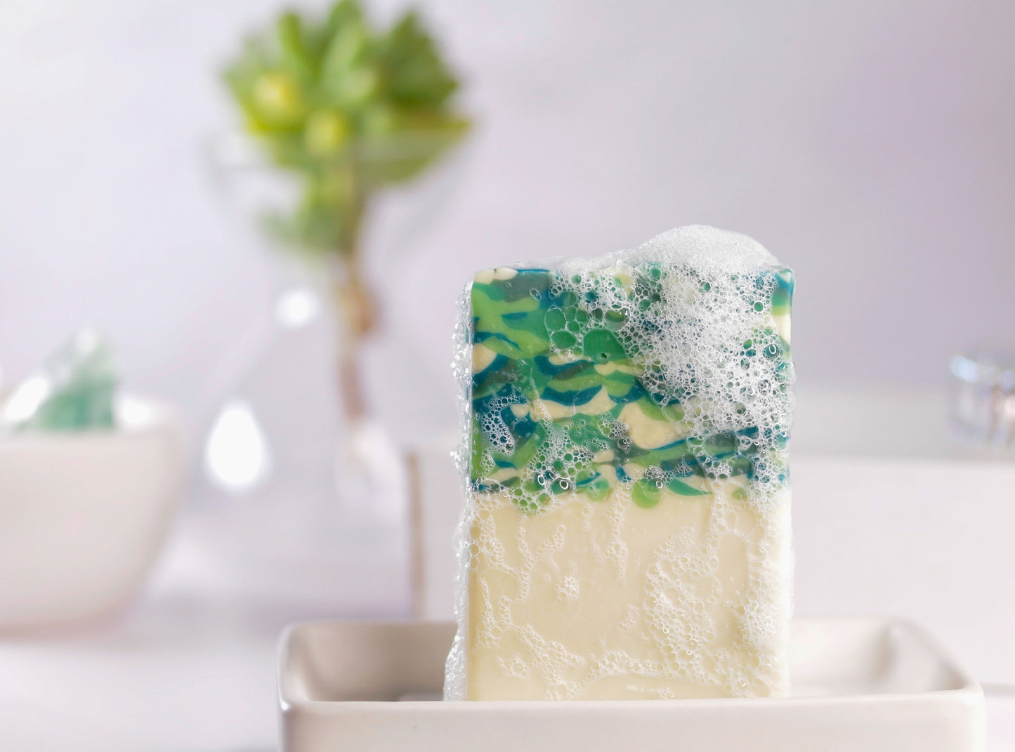 Bar of soap with green and blue marbled design in a white dish on a light background