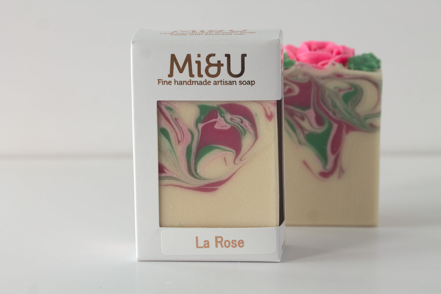 Marbled soap with pink and green swirls next to a Mi&U branded box on a white background