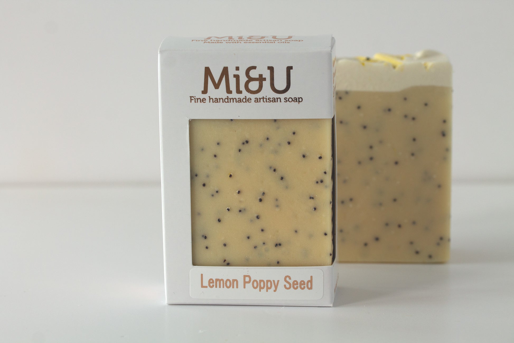 Bar of soap with lemon poppy seed scent next to its packaging on a white background