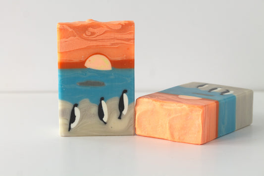 Two soap bars with penguins on a beach on a white background