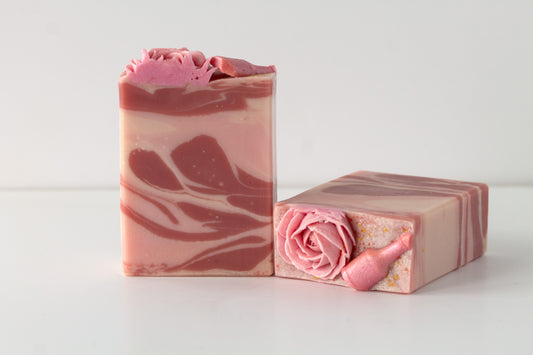 Two pink marbled soap bars with floral designs and champagne bottles on a white background