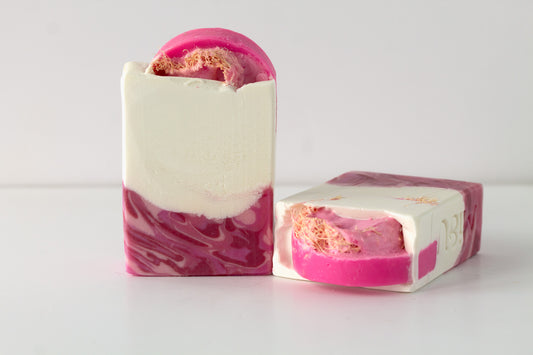 Two pomegranate  loofah soap bars with pink and white marbled swirls on a light surface