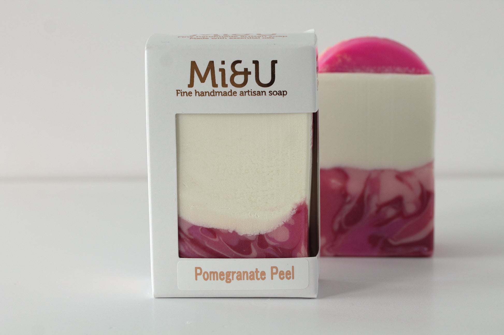 Mi&U handmade pomegranate loofah artisan soap with pink and white swirls next to its packaging on a white background