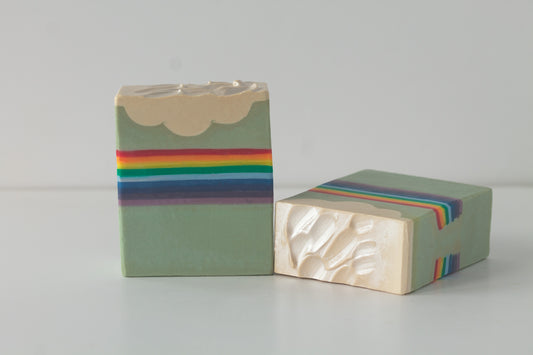 Two rainbow soap bars with cloudy tops on a white surface