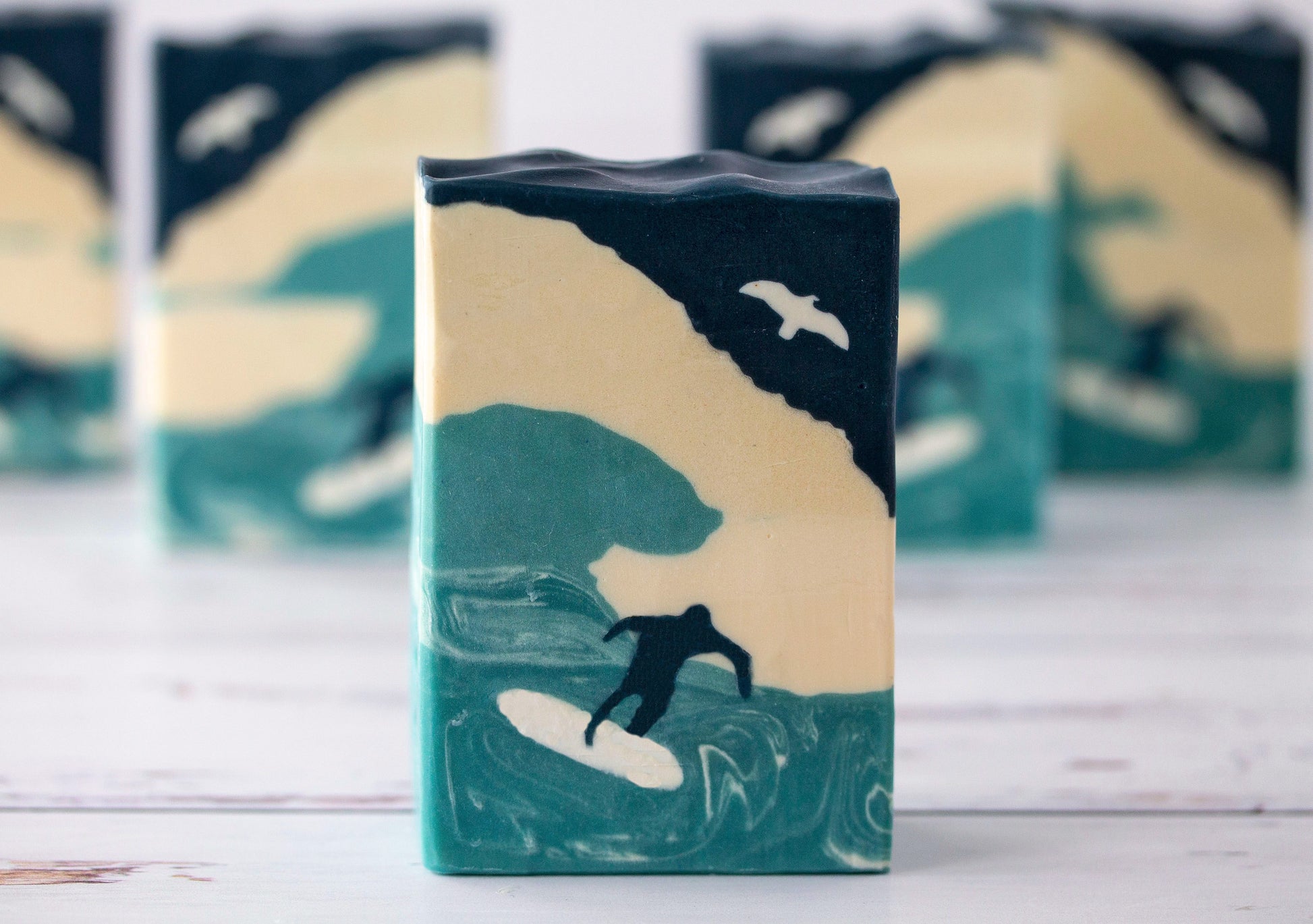 Bar of soap with a design of a surfer and ocean waves on a wooden surface.